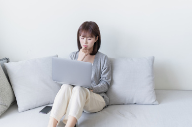 亚洲女生坐在沙发上一边看电脑一边思考