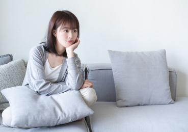 年轻的亚洲女生盘腿坐在沙发上托腮思考