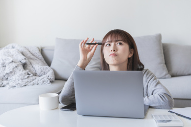 女生在手提电脑前用笔抵着脑袋在思考