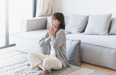 女生坐在客厅地毯上双手合十闭眼祈祷