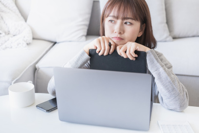 女生在电脑前将下巴抵在本子上思考