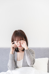 坐在床上一边接电话一边揉眼睛的亚洲女性