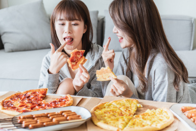 两位年轻亚洲女孩在客厅吃披萨