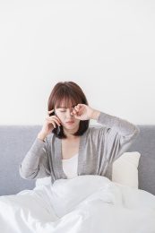 坐在床上一边接电话一边揉眼睛的亚洲女性