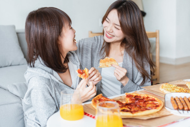 两位年轻亚洲女孩在客厅吃披萨