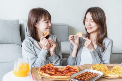 两位年轻亚洲女孩在客厅吃披萨