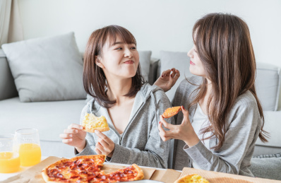 两位年轻亚洲女孩在客厅吃披萨