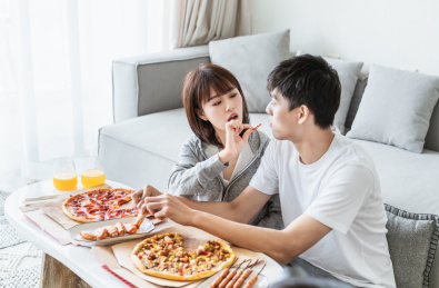 年轻情侣在客厅一边打闹一边吃披萨