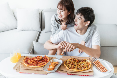 年轻情侣在客厅一边打闹一边吃披萨