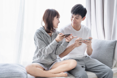 年轻情侣坐在窗边一起玩手机游戏