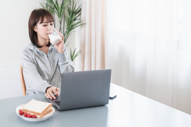 年轻女性一边喝牛奶一边看电脑