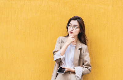 年轻女生在黄色背景墙前托下巴思考