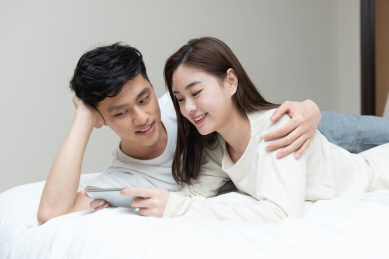 一对年轻的亚洲情侣正在床上玩手机