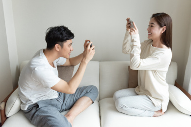 一对年轻的亚洲情侣在沙发上互相拍照