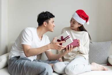 一对年轻的亚洲情侣在沙发上互送礼物