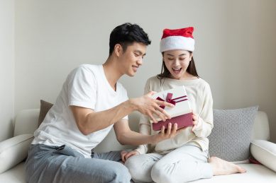 一对年轻的亚洲情侣在沙发上互送礼物