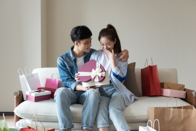 一对年轻的亚洲情侣在沙发上互送礼物