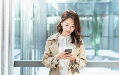 亚洲商务人士靠在窗边栏杆低头看手机