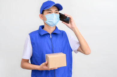 白色背景前带着口罩打电话的快递员