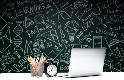 黑板画前的桌子上笔记本电脑和文具