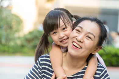亚洲母女在户外，妈妈背着小女孩开心笑着