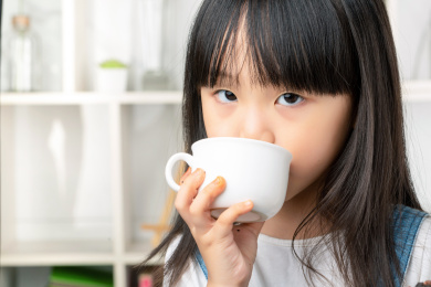 拿着白色杯子喝水的亚洲小女孩