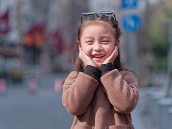阳光下的中国小女孩手捂脸笑看着镜头