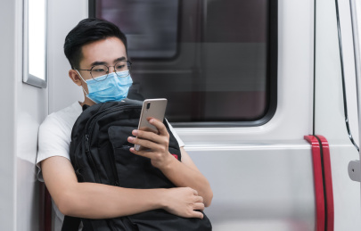 戴口罩的年轻男子在地铁里坐着玩手机