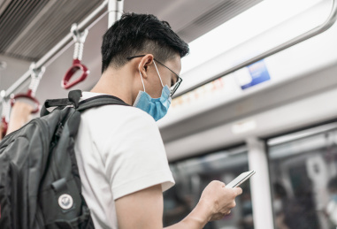戴着口罩在地铁内看手机的亚洲男青年