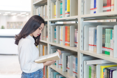 图书馆书架前一个漂亮的女大学生在看书