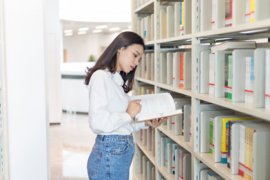 图书馆书架前一个漂亮的女大学生在看书