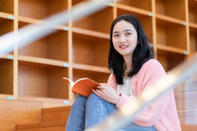 年轻学生坐在图书馆台阶上看着前方