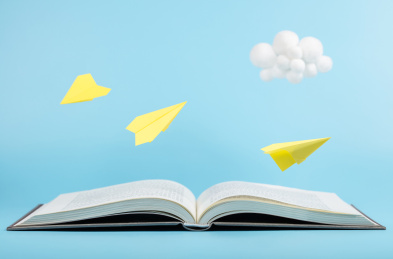 蓝色天空书本上飞翔的纸飞机与可爱的云朵