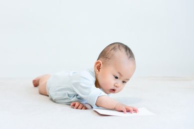 趴在床上手玩白色卡片的9个月婴儿