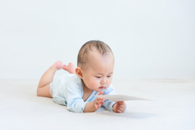 趴在床上手玩白色卡片的9个月婴儿