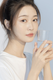 身穿白T恤的马尾女孩拿着玻璃水杯看前方