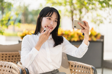 亚洲商务女士在户外对着手机补口红