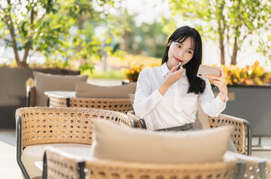 商务女性坐在室外对着手机补口红