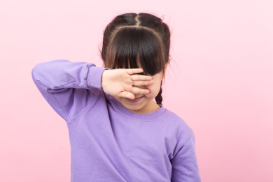 粉色背景前捂着眼睛哭泣的亚洲小女孩