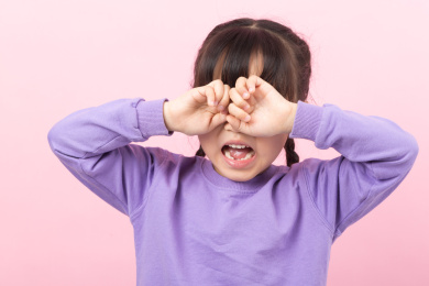 粉色背景前捂着眼睛哭泣的亚洲小女孩