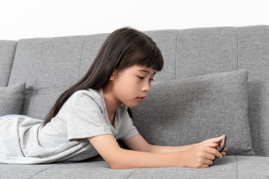 客厅沙发上一个中国小女孩趴着玩手机